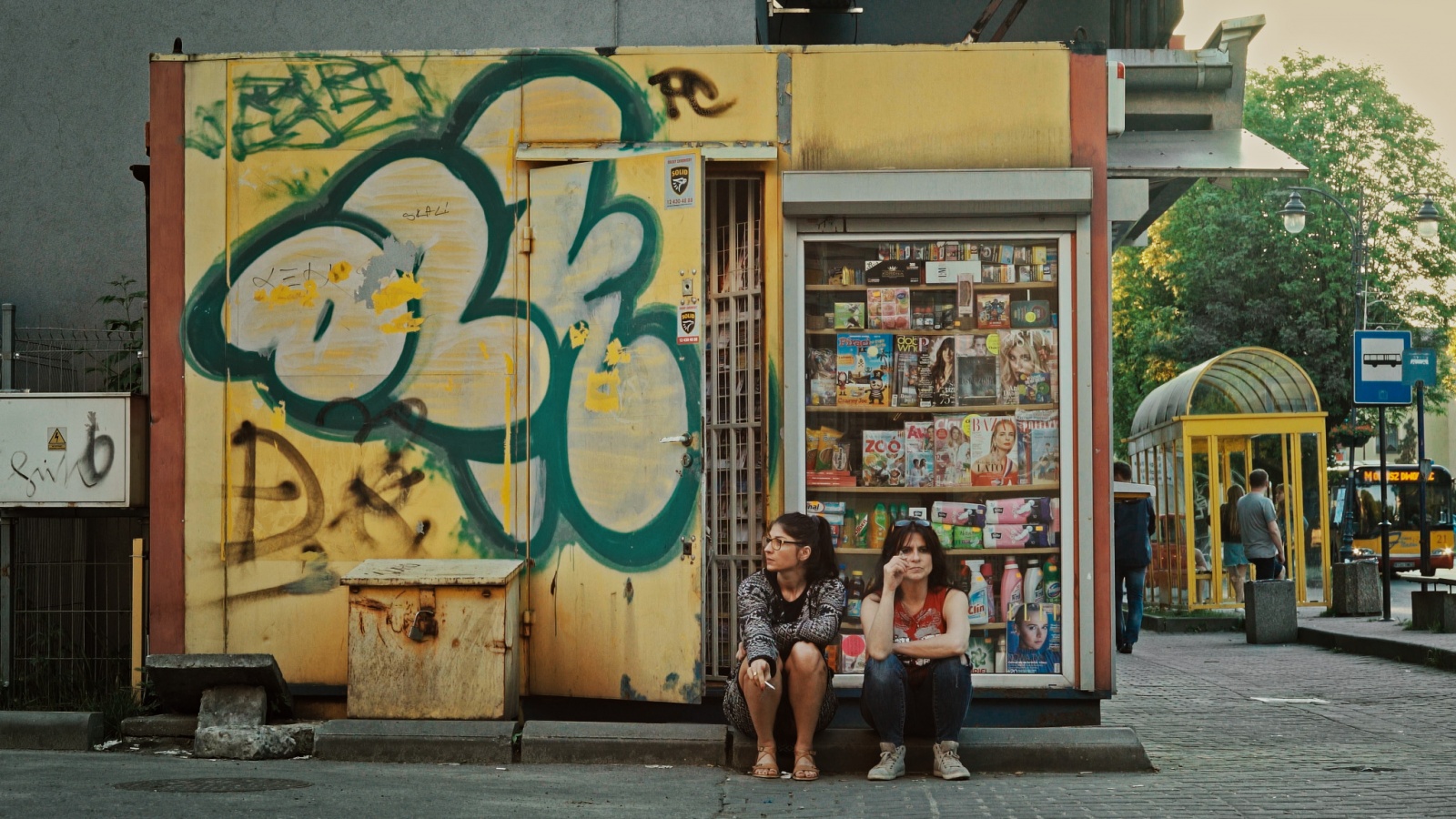 eng: Two women are sitting near a kiosk.