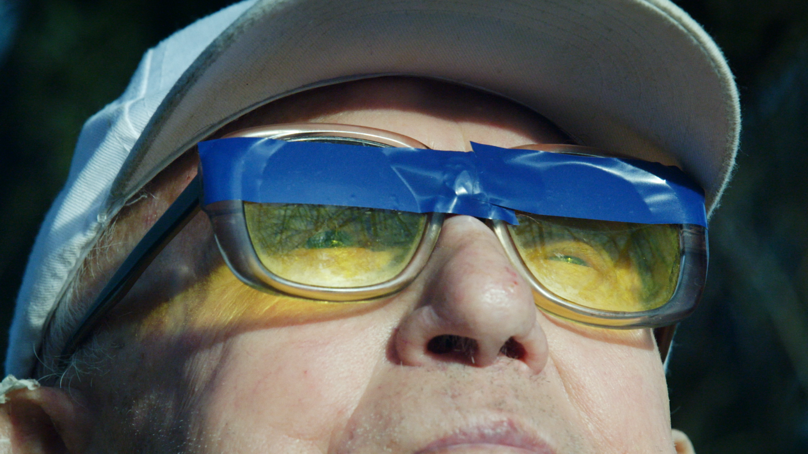 eng: Old man looks through yellow glasses covered with a blue patch.